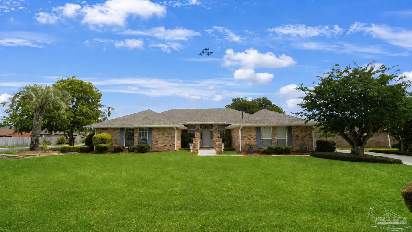 Single-story brick home with a large green lawn, palm tree, and a formation of fighter jets flying in the blue sky.
