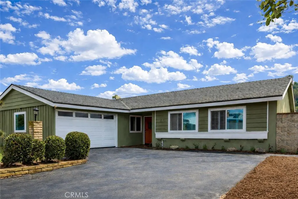 Olive green single-story home with a gray roof, white garage door, and an orange front door under a blue sky.