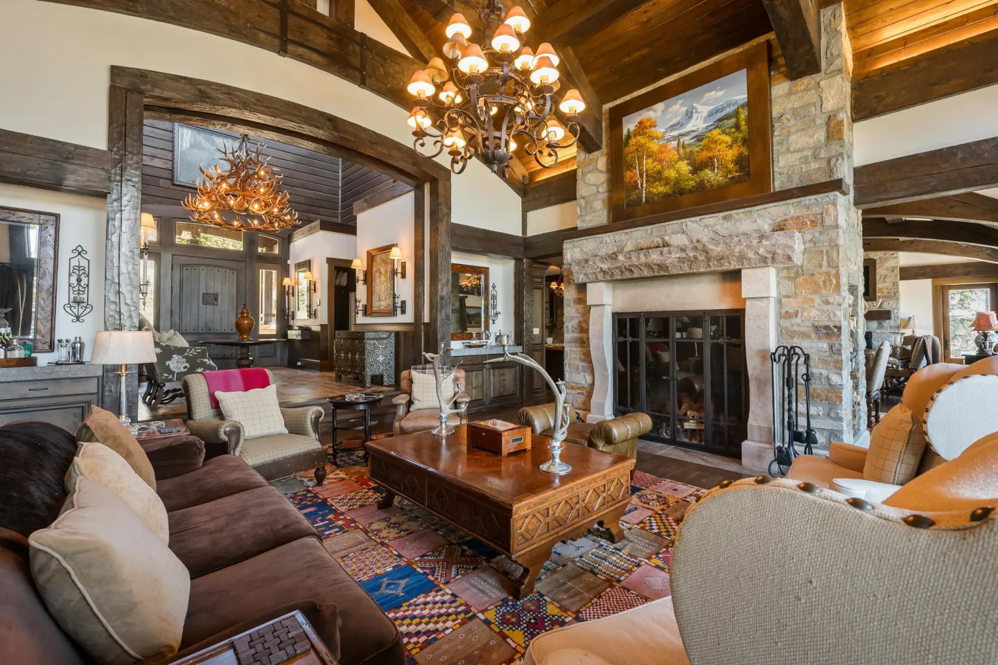 A spacious living room with a stone fireplace, wooden beams, and a colorful patchwork rug.