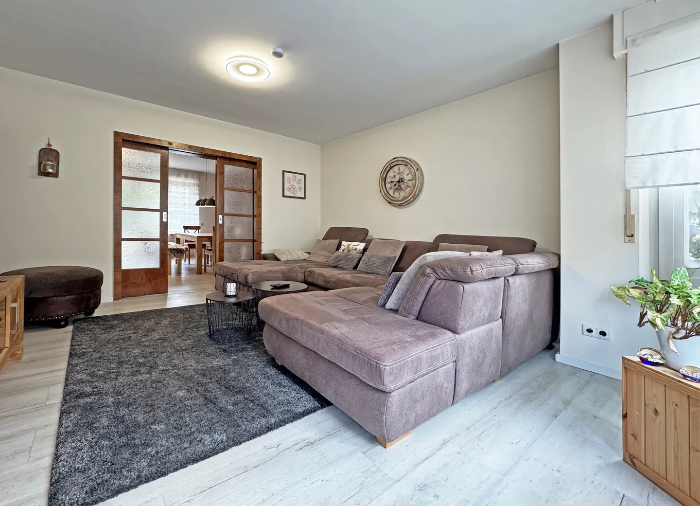 Living room with a large brown sectional sofa, gray rug, and wood-framed glass doors leading to a dining area.
