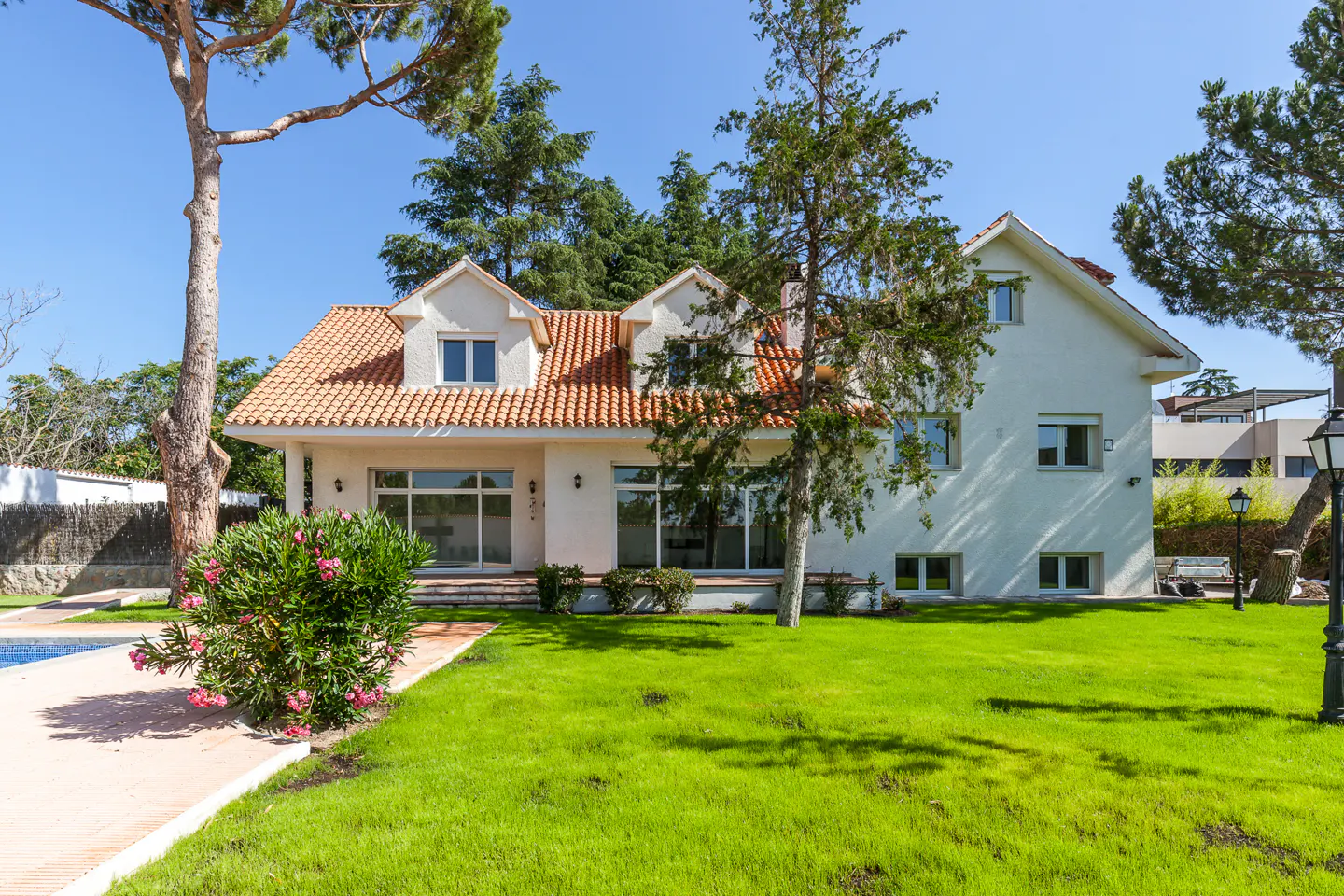 Two-story white house with a terracotta roof, large windows, and a lush green lawn under a clear blue sky.