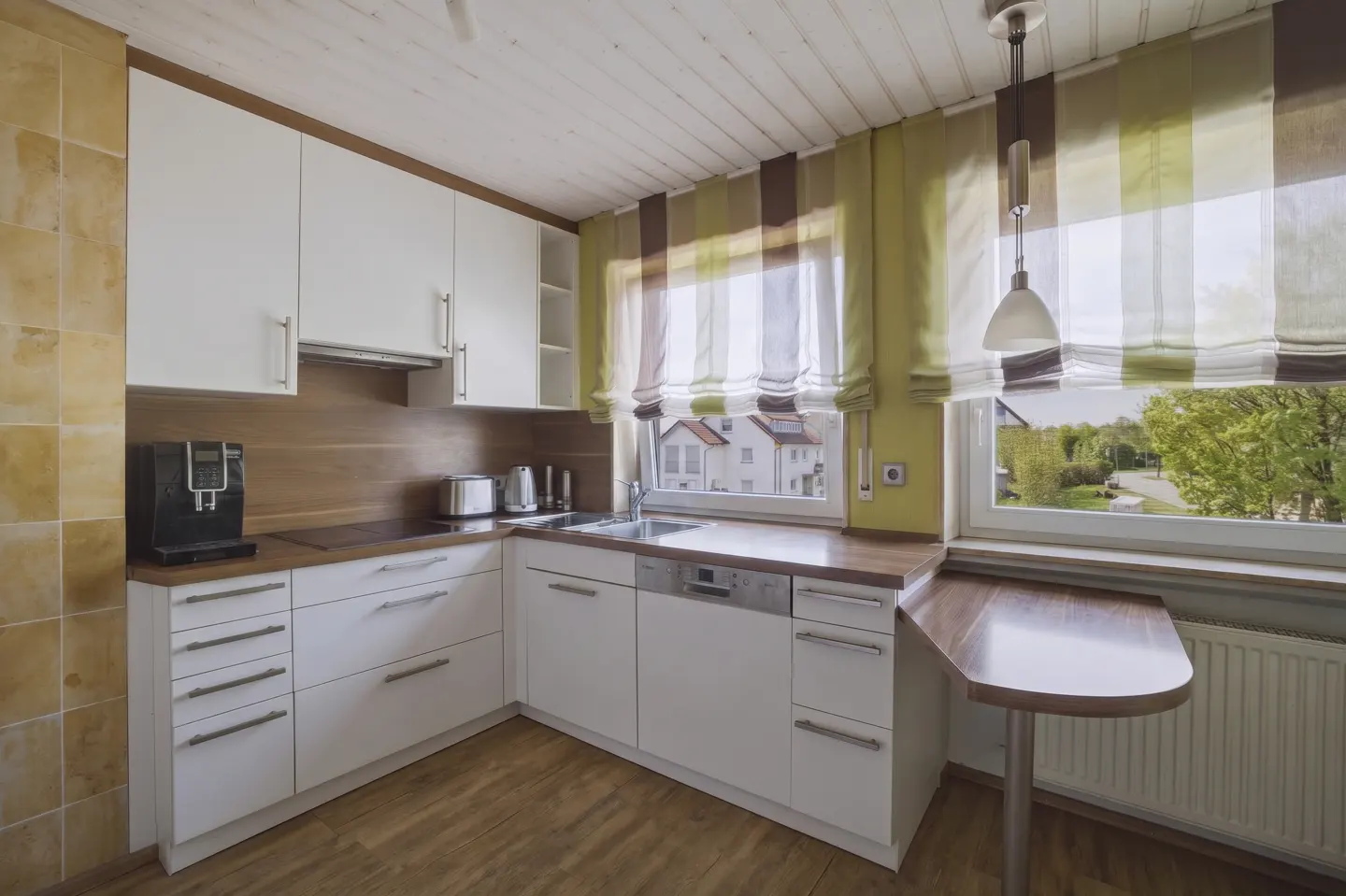 Modern kitchen with white cabinets, wood countertops, a small breakfast bar, and windows with green-striped curtains.