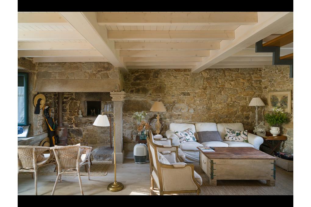 Rustic living room with stone walls, exposed wooden ceiling beams, white sofa, wicker chairs, and a wooden coffee table.