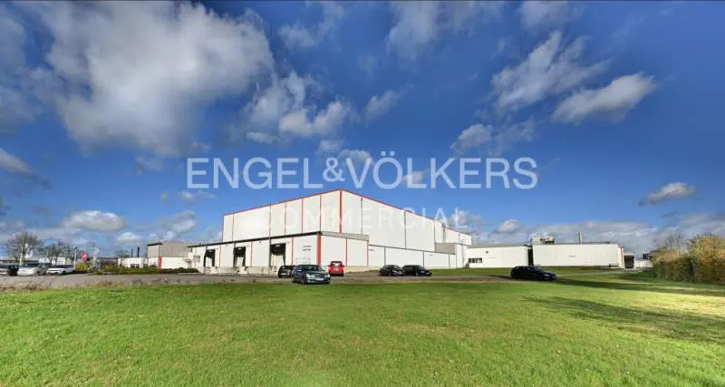 Exterior of a large, white commercial building with red trim, under a blue sky with scattered clouds. Cars are parked in front.