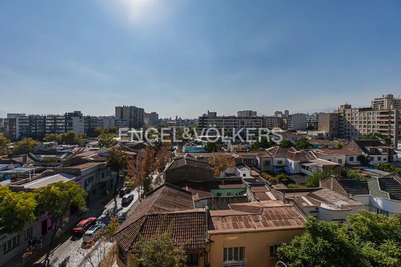 Cityscape view with red-roofed houses, green trees, and tall buildings under a bright blue sky.