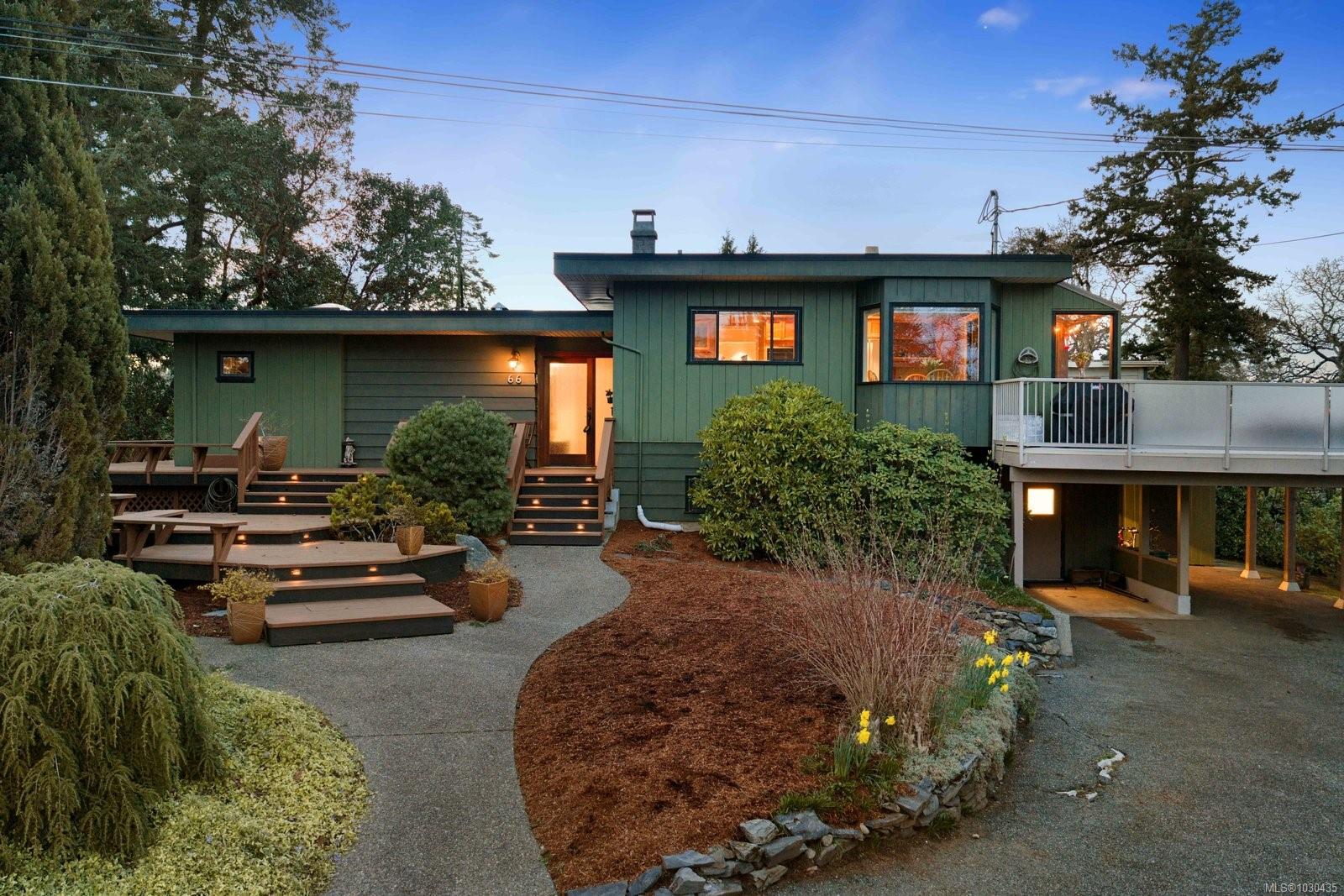 Exterior of a green, modern home with a deck, landscaped yard, and a winding walkway leading to the front door.