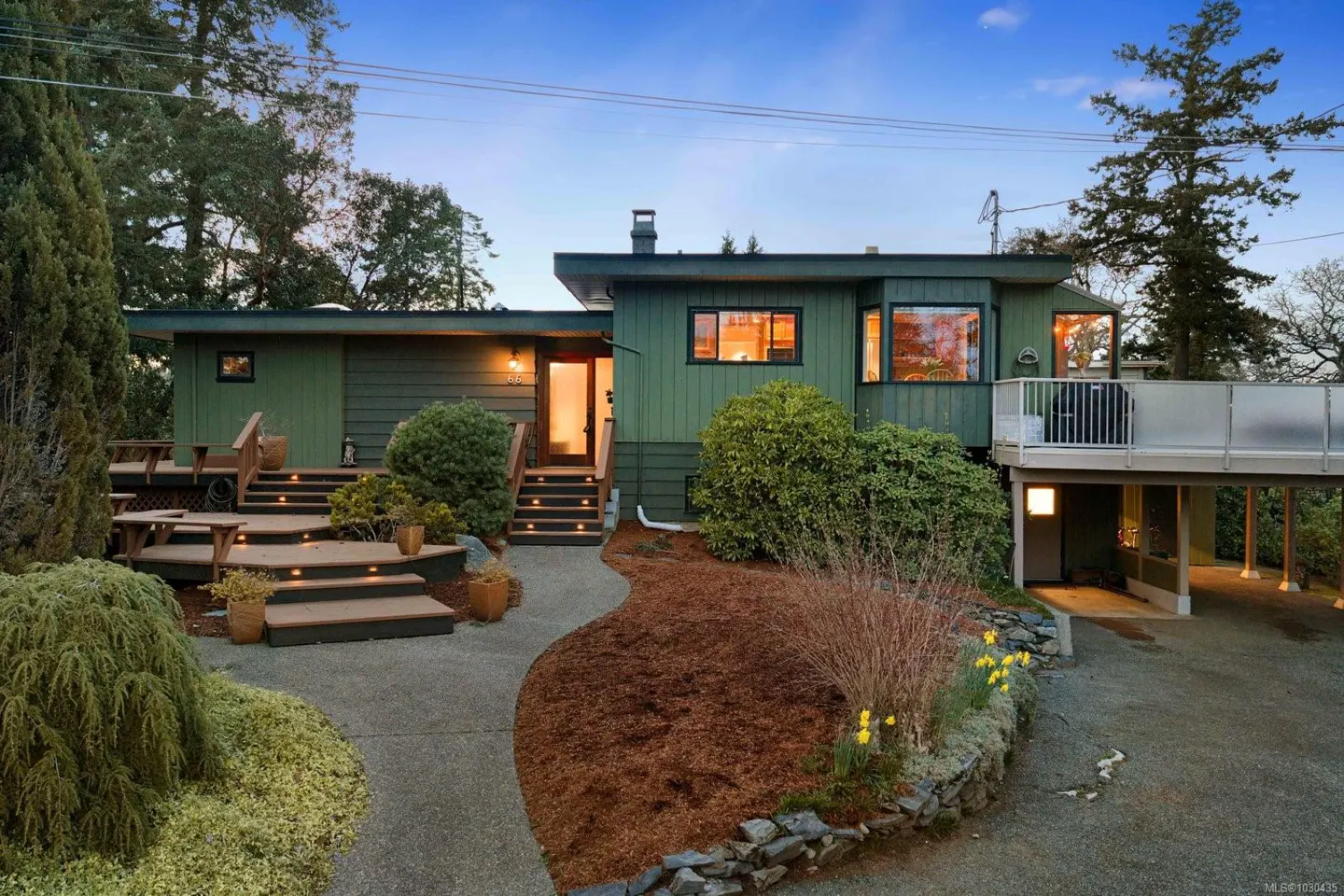 Exterior of a green, modern home with a deck, landscaped yard, and a winding walkway leading to the front door.