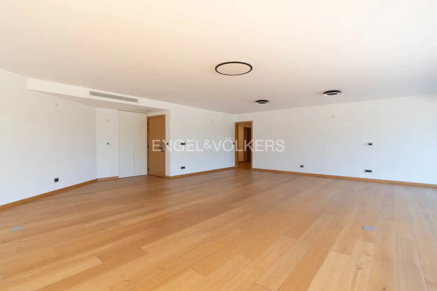 Bright, empty room with light wood floors, white walls, and recessed lighting. Engel & Völkers logo is visible.
