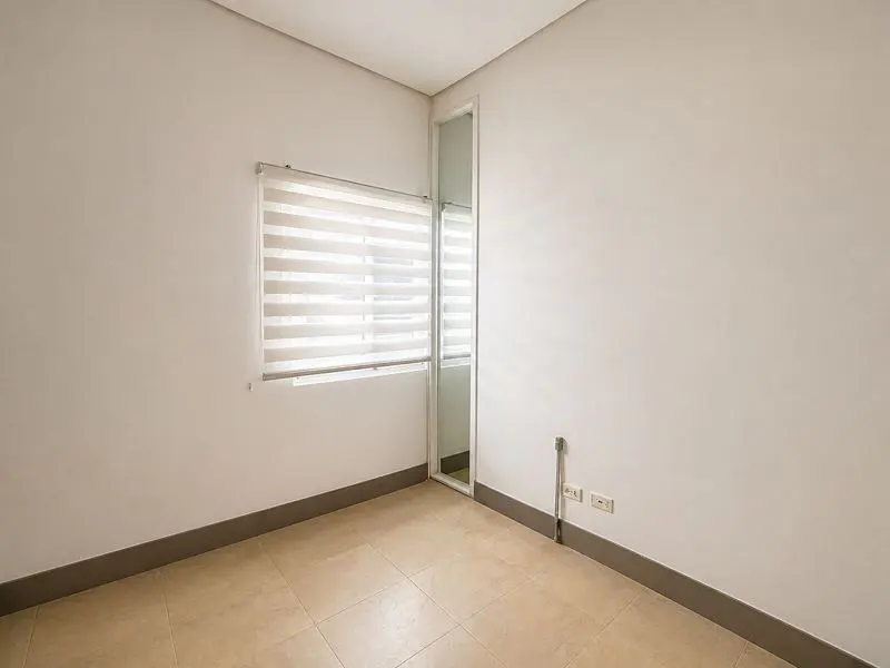 Empty room with beige tile floor, white walls, and a window with horizontal blinds. A narrow doorway is next to the window.