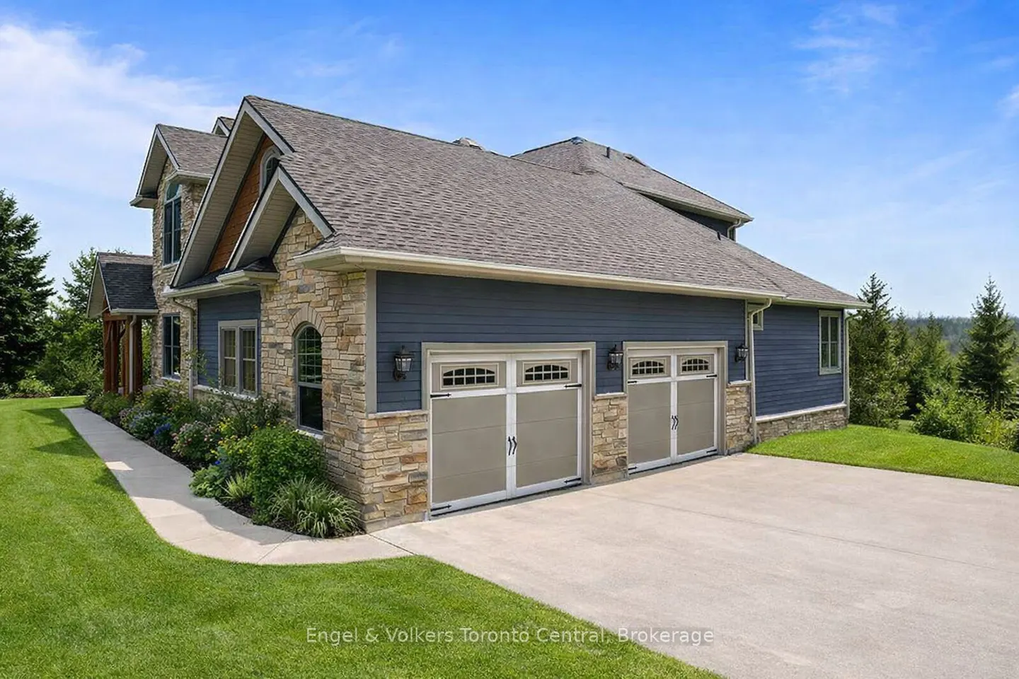 Exterior view of a two-story house with blue siding, stone accents, and a two-car garage under a blue sky.