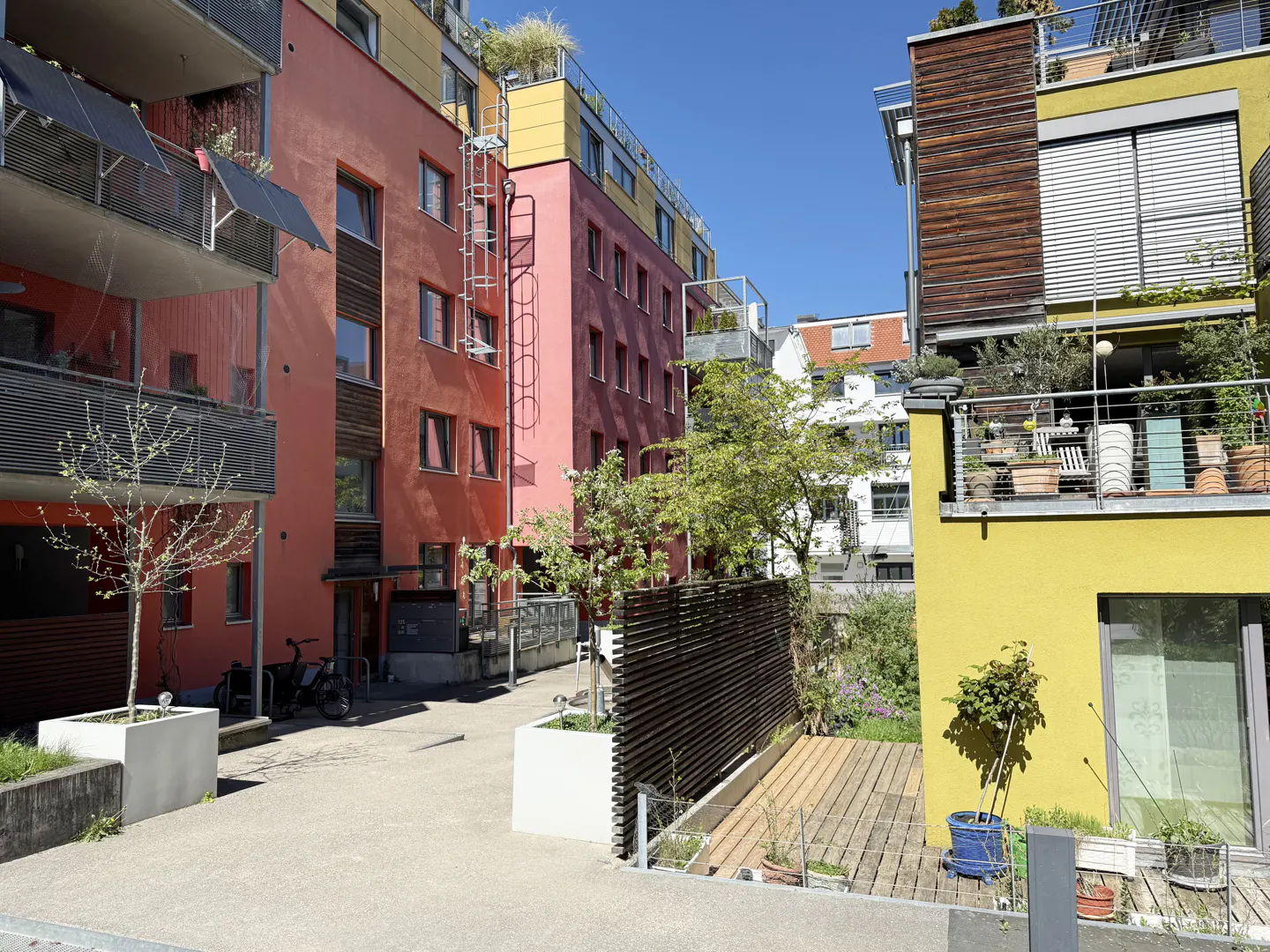 Exterior view of colorful modern apartments with balconies and greenery under a blue sky.