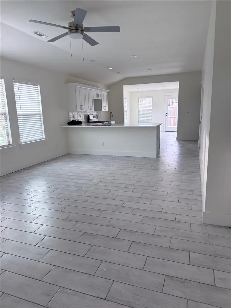 Bright, open-concept living space with white walls, gray tile floors, and a kitchen with white cabinets and a breakfast bar. A ceiling fan is visible.