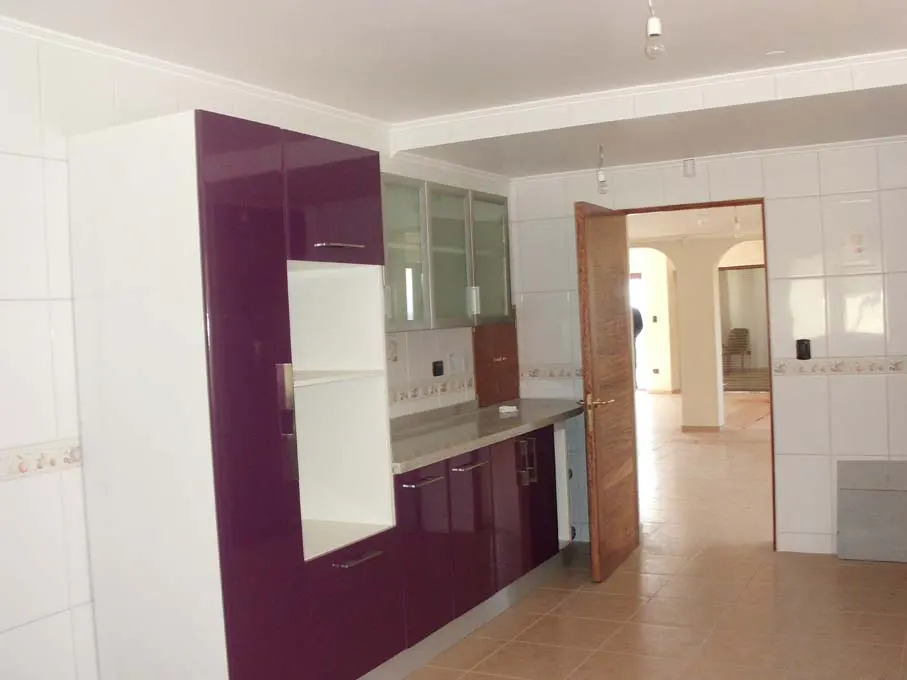 A bright kitchen with white tile walls, purple and white cabinets, and a doorway to another room.