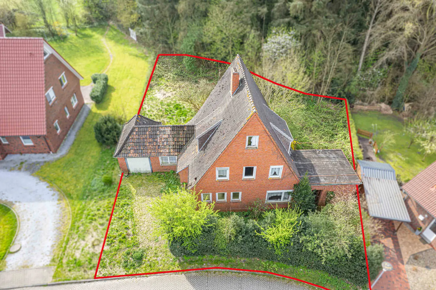 Aerial view of a red brick house with a dark roof, surrounded by a red boundary line and greenery.