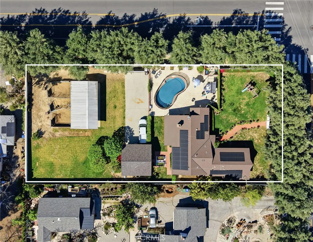Aerial view of a property with a house, pool, barn, and green lawn, surrounded by trees and a white border.