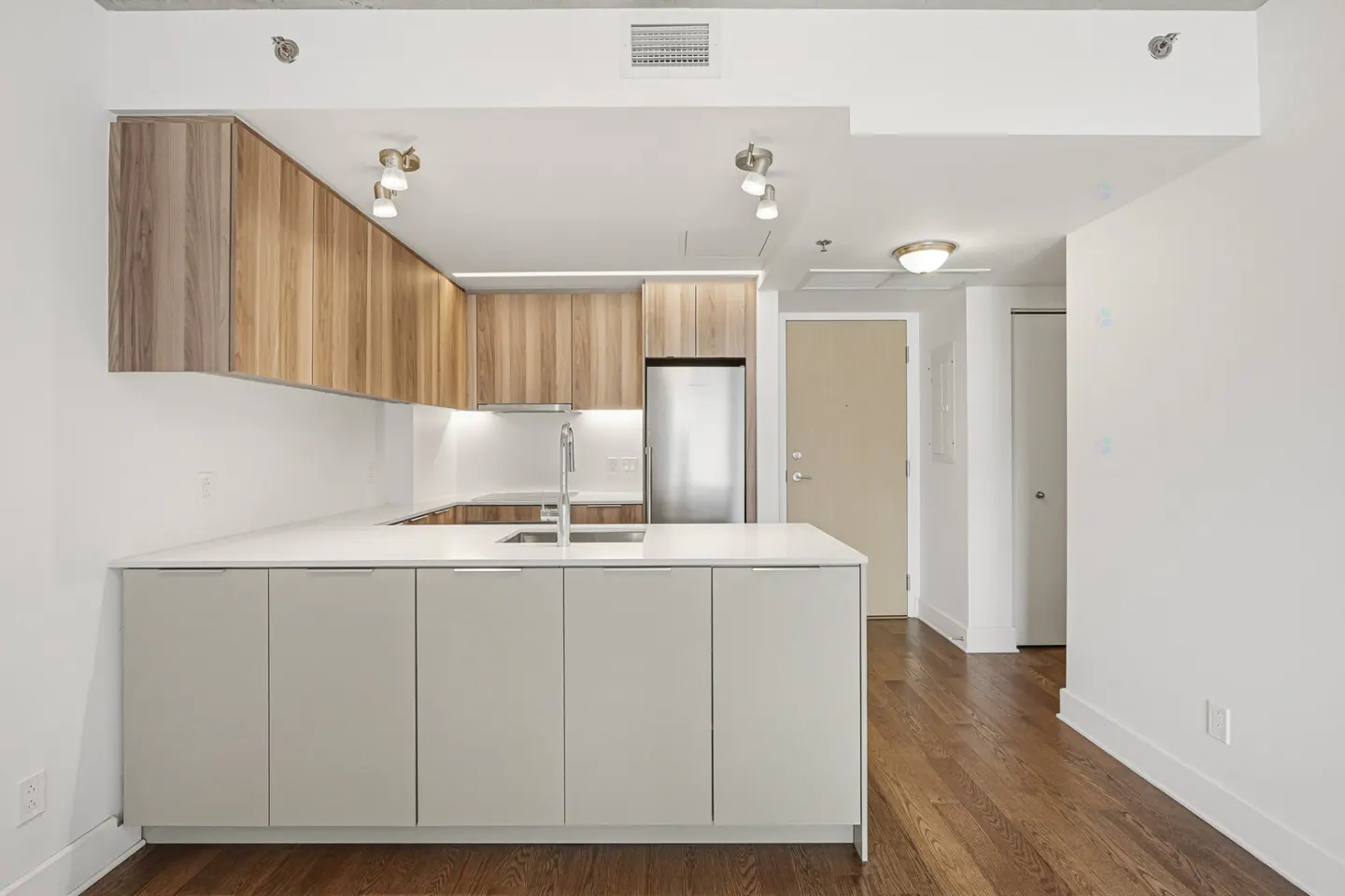 A modern kitchen with wood and gray cabinets, white countertops, stainless steel appliances, and dark wood floors.
