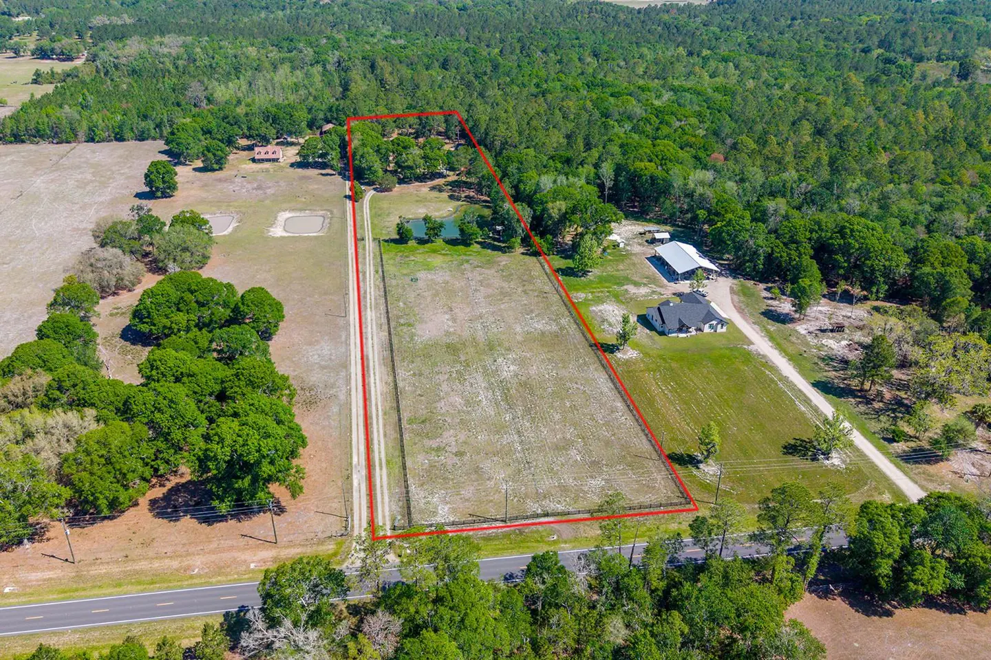 Aerial view of a large, rectangular property outlined in red, featuring a field, ponds, homes, and surrounding green trees.