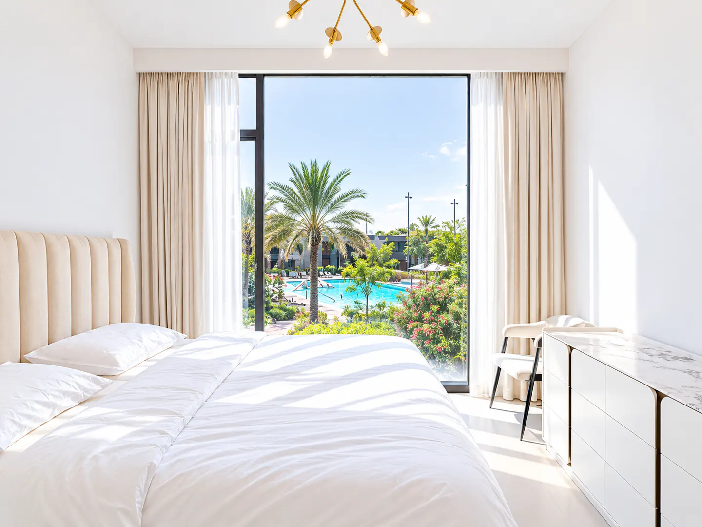 Modern bedroom with a large window overlooking a sunny resort pool, palm trees, and lush landscaping.