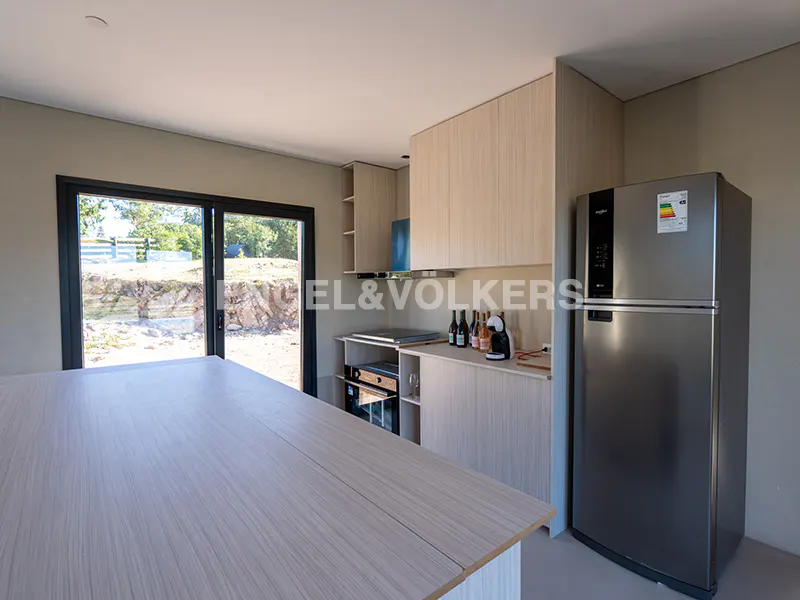 Bright kitchen with light wood cabinets, stainless steel refrigerator, and a large island. Sliding glass doors offer a view of the outdoors.