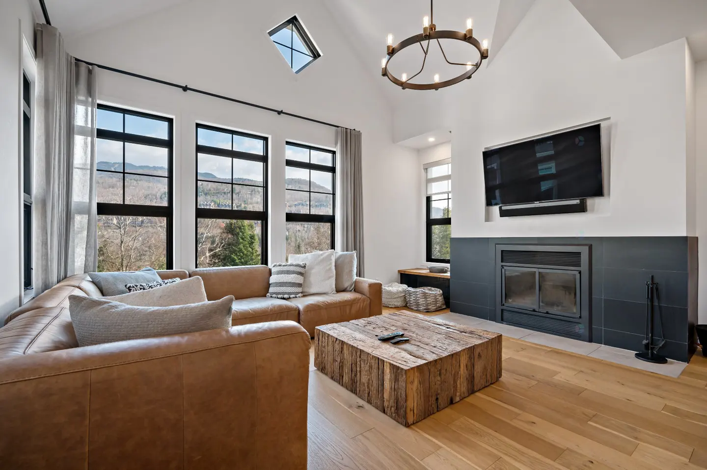 Living room with tan leather sectional, wood coffee table, fireplace, and large windows with mountain views.