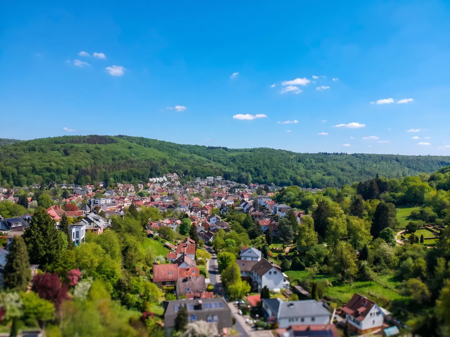 Aerial view of a town nestled in a lush green valley under a bright blue sky with scattered white clouds.