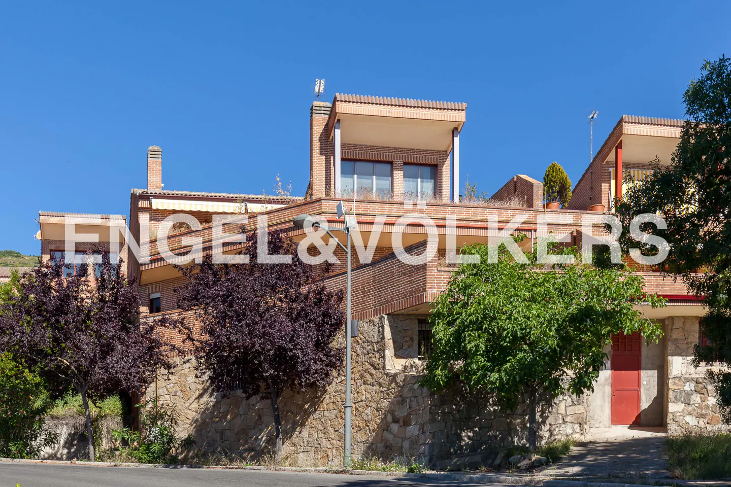 Exterior view of a brick house with a red door, trees, and an Engel & Volkers logo overlayed on the image.