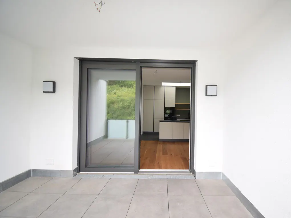 View from a tiled patio through sliding glass doors into a modern kitchen with white cabinets and wood floors.