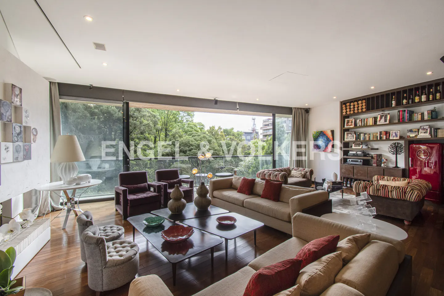 A spacious living room with hardwood floors, sofas, chairs, and a large window overlooking trees.