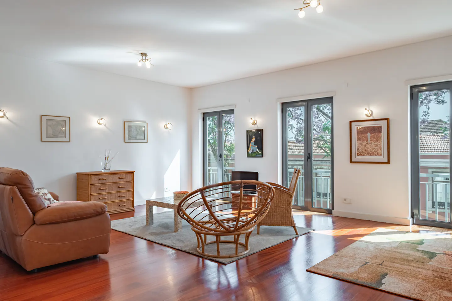 Bright living room with hardwood floors, a brown leather recliner, rattan chairs, and glass doors leading to a balcony.