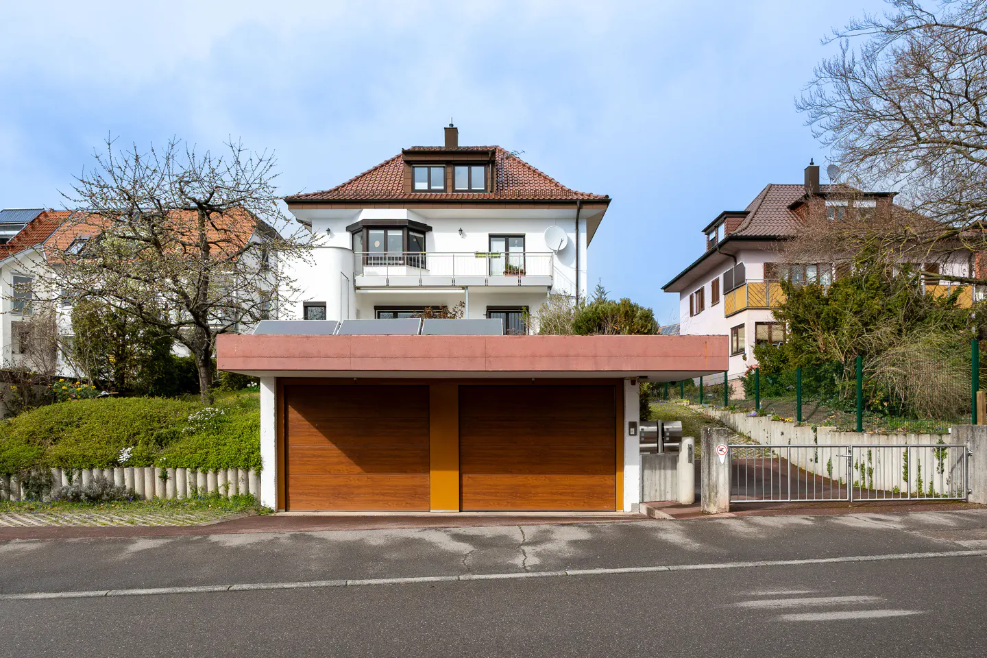 A two-car garage with brown doors sits in front of a white house with a red tile roof.