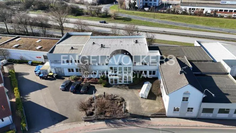 Aerial view of the Engel & Volkers Commercial building, a light gray structure with a curved glass entrance, surrounded by parking and greenery.