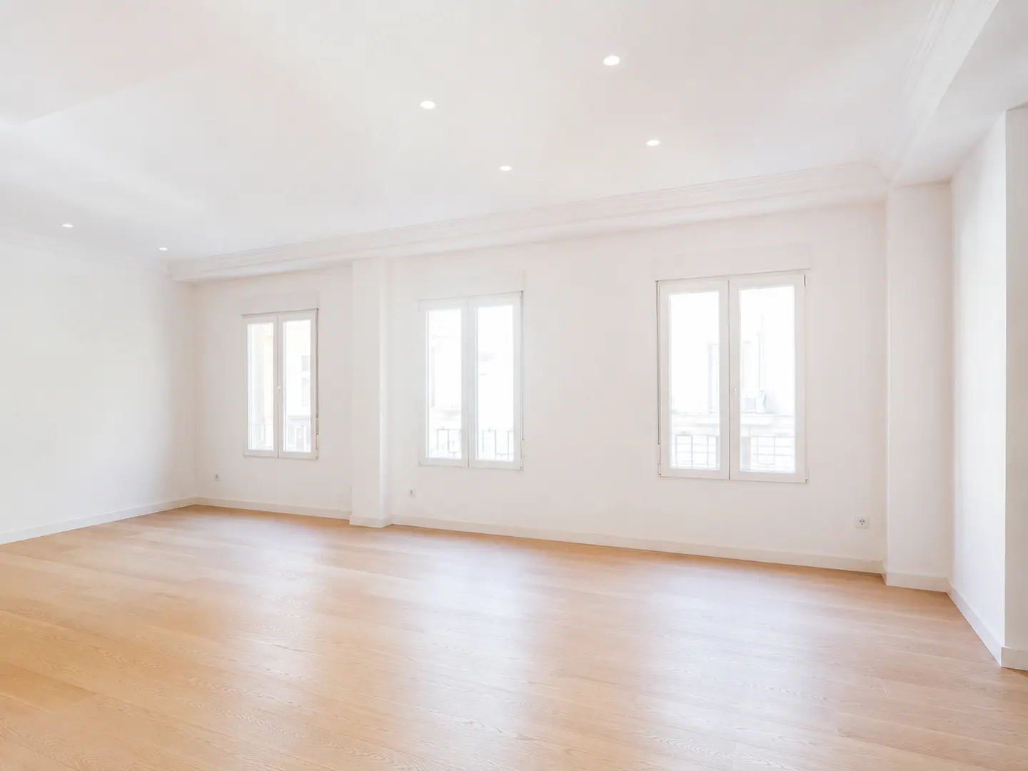 Bright, empty room with light wood floors, white walls, and three windows letting in natural light.