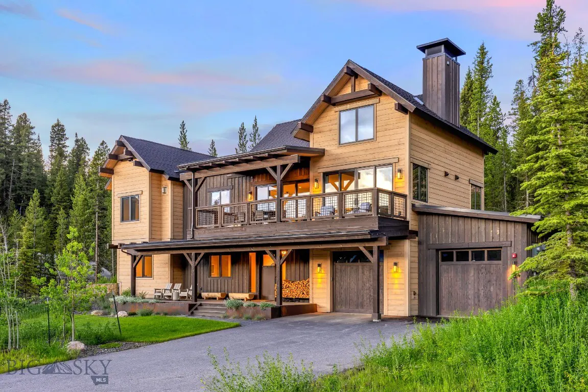 Two-story tan house with a dark roof, a balcony, and a garage, surrounded by green grass and trees.