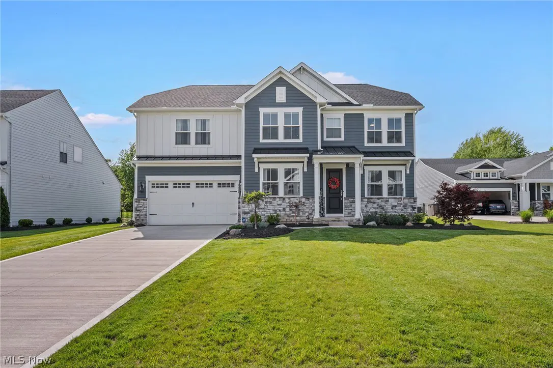 Two-story house with blue siding, white trim, and a gray roof on a green lawn under a blue sky.