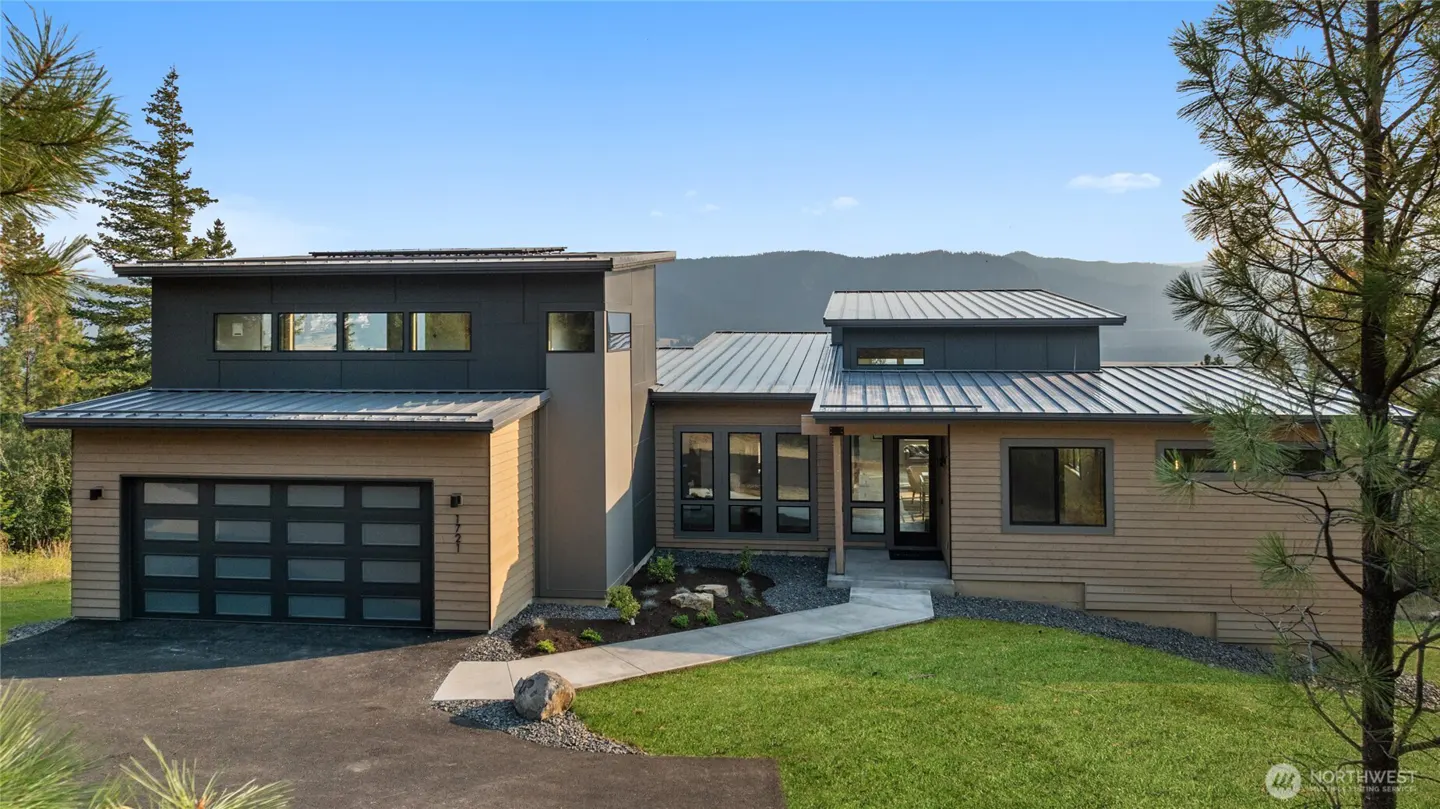 Exterior of a modern two-story home with a gray roof, tan siding, black garage door, and a concrete walkway.