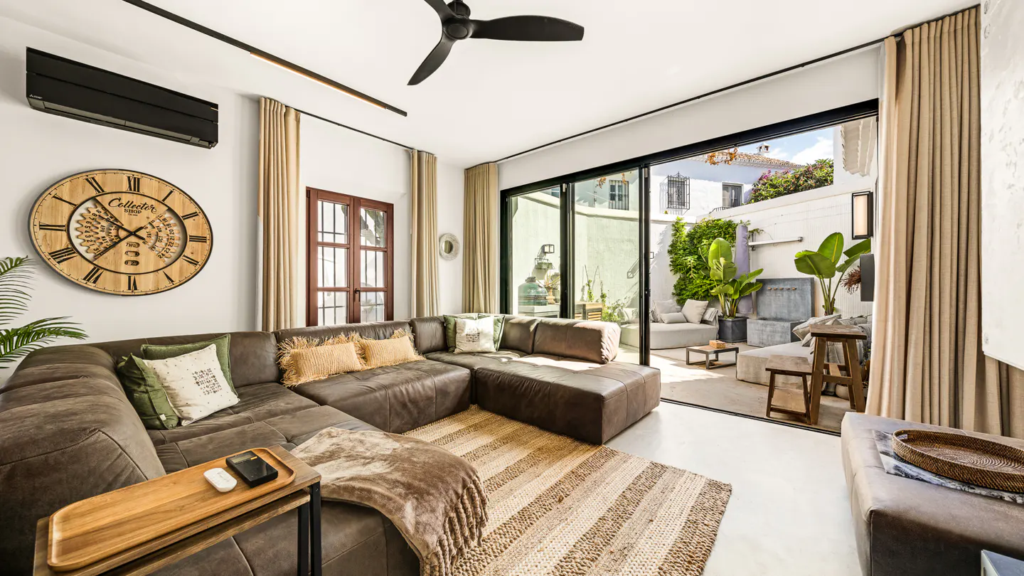 Living room with a brown leather sectional sofa, a large clock on the wall, and sliding glass doors to a patio.