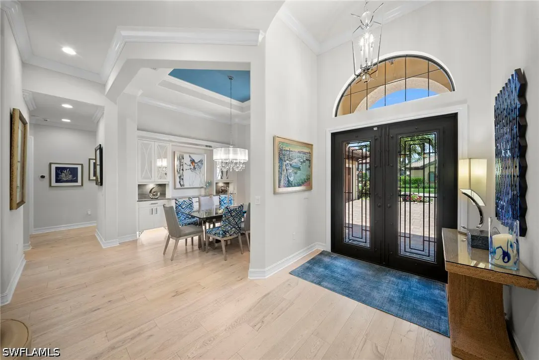 Bright foyer with light wood floors, black double doors, and a blue rug. A dining area is visible through an archway.