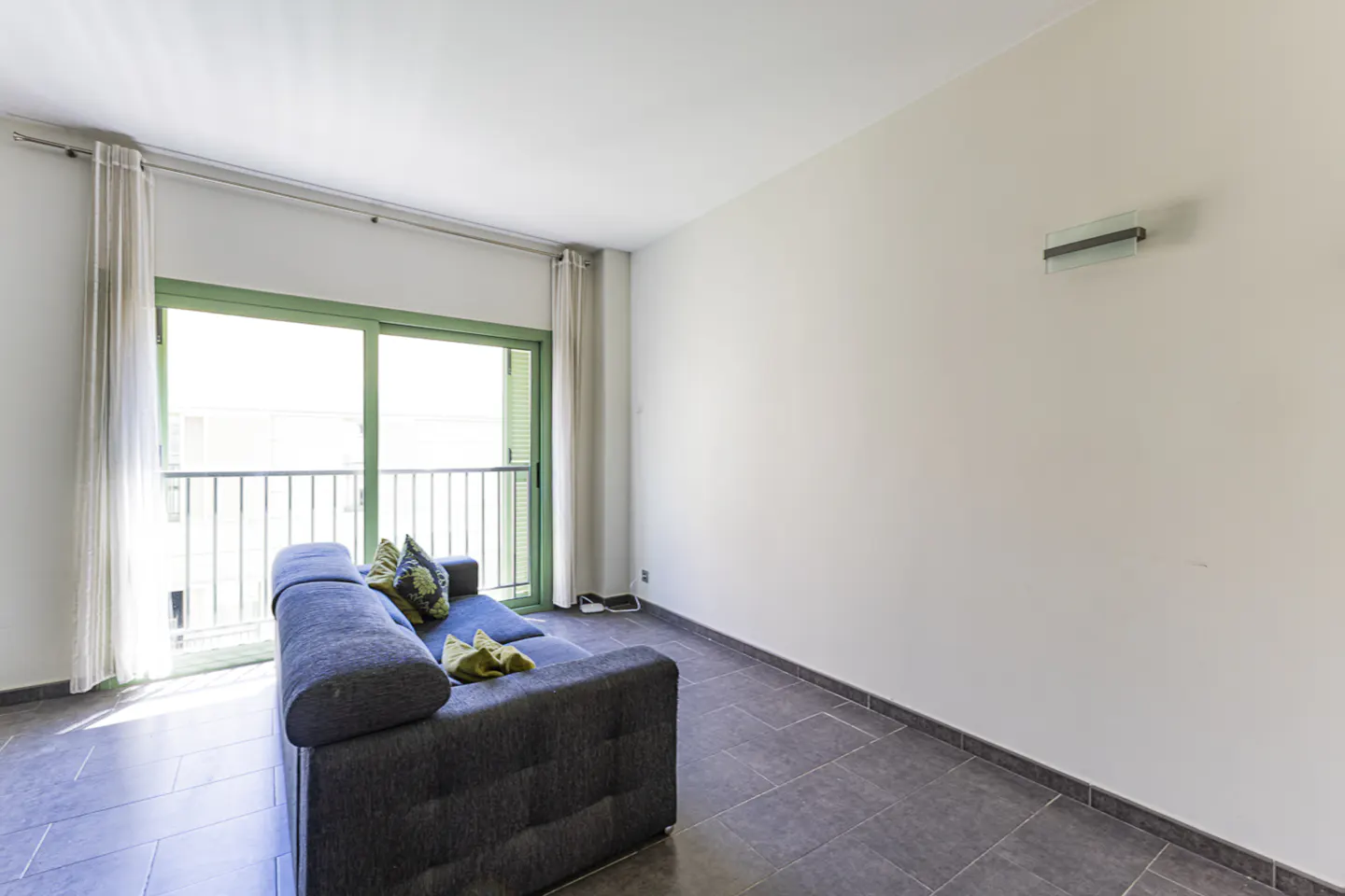 Living room with a gray sofa, green pillows, and a balcony with green frame. The floor is tiled in gray.