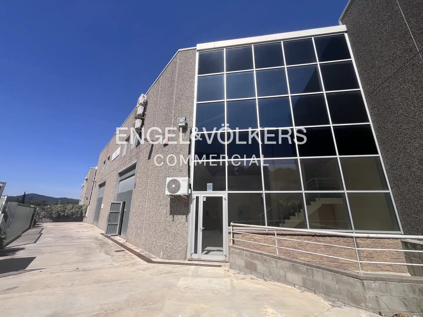 Exterior view of a commercial building with large windows, the Engel & Völkers logo, and a blue sky.