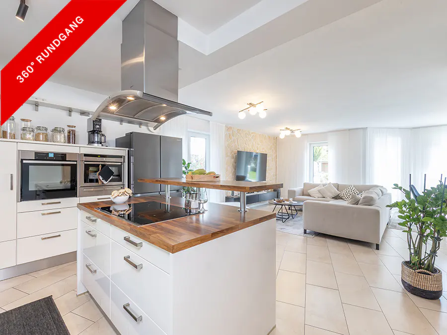 Open-concept kitchen and living room with white cabinets, wood countertops, stainless steel appliances, and a gray sofa.
