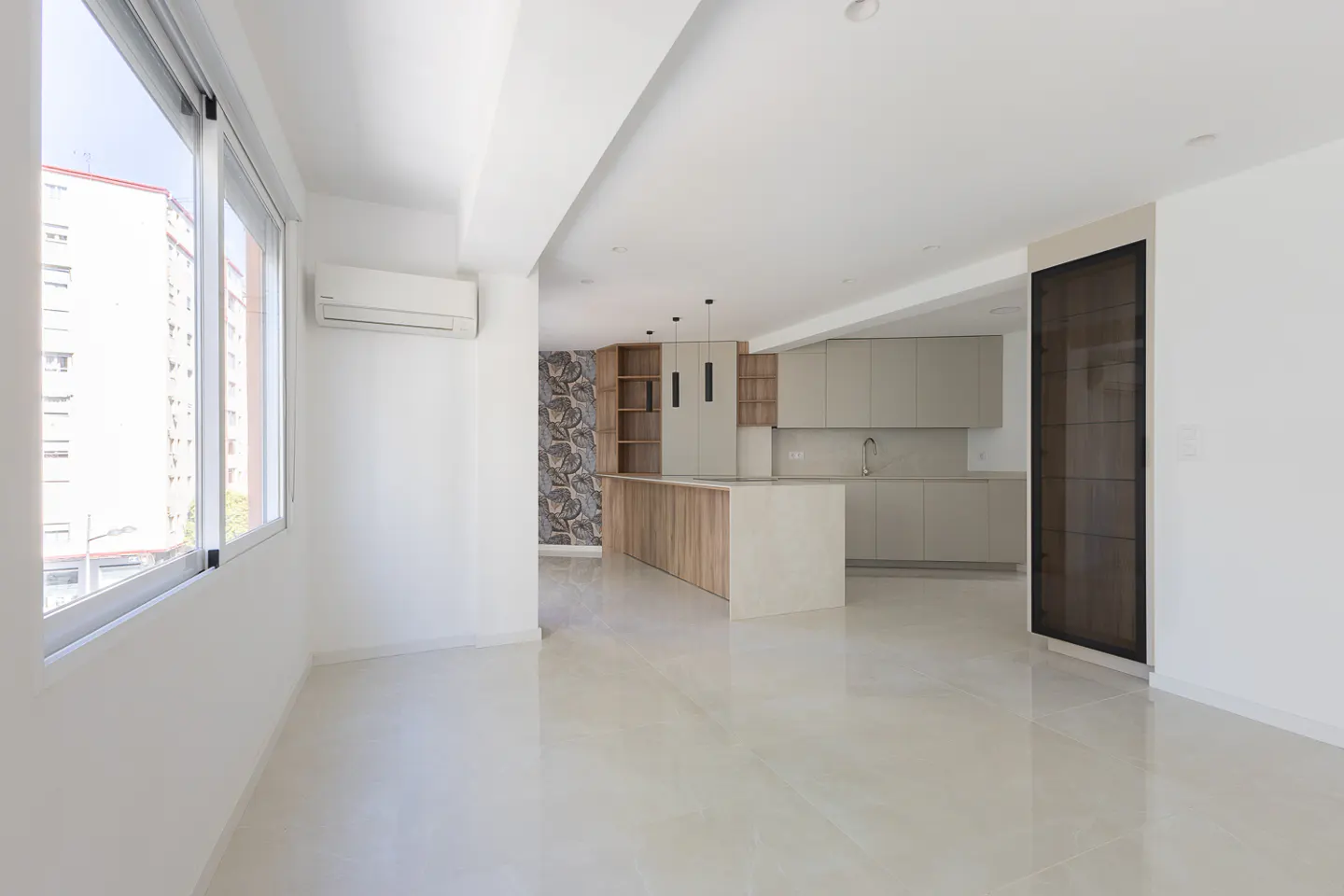 Bright, modern apartment interior with white walls, tile floors, and a kitchen with wood island and gray cabinets. Large windows offer city views.
