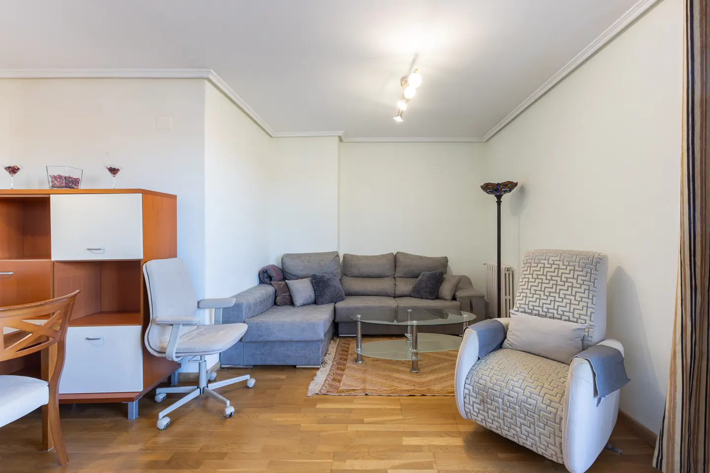 Living room with gray sectional sofa, patterned armchair, glass table, and wood floors.