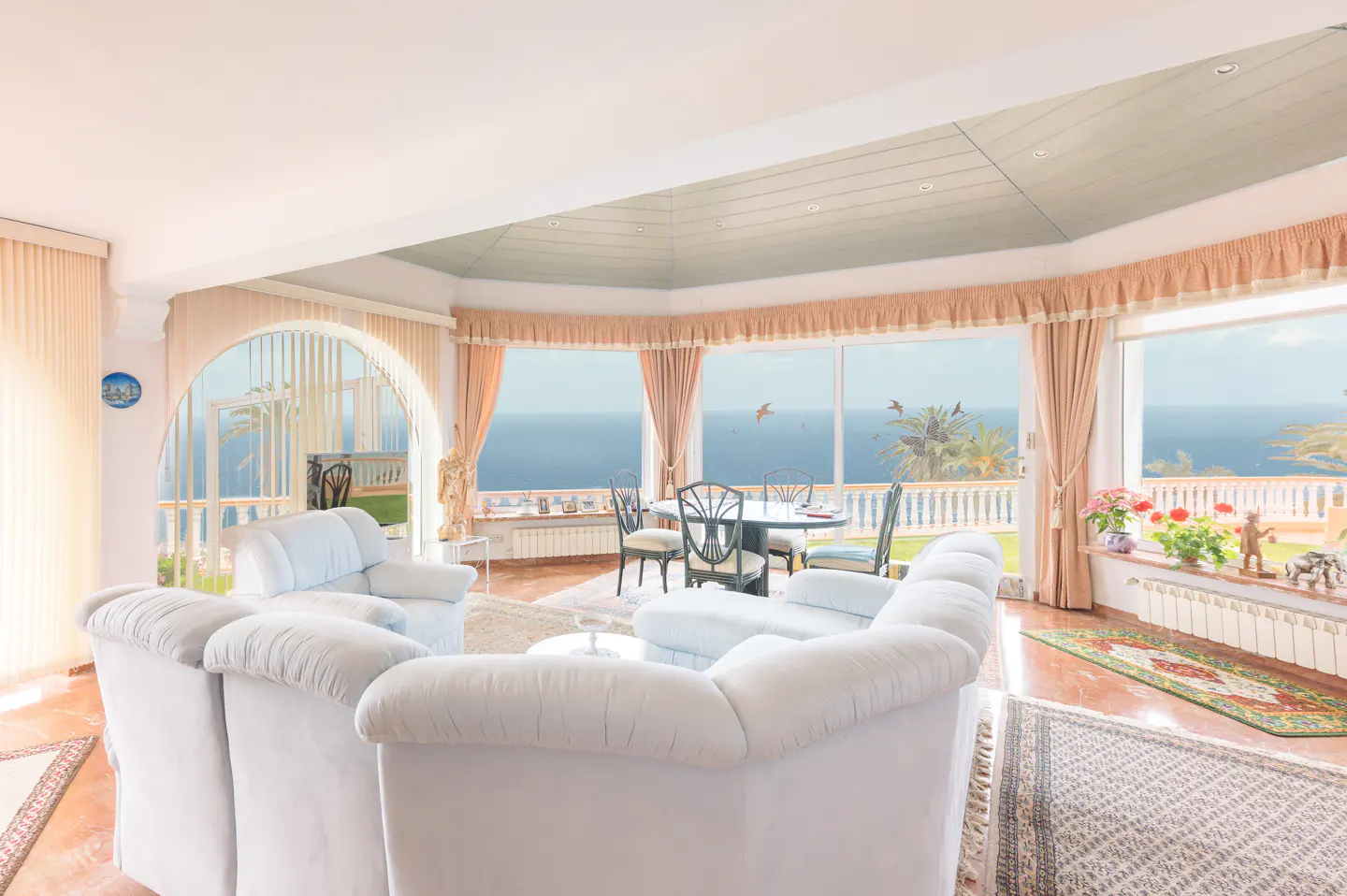 Bright living room with white sofas, a round table, and large windows overlooking the ocean.