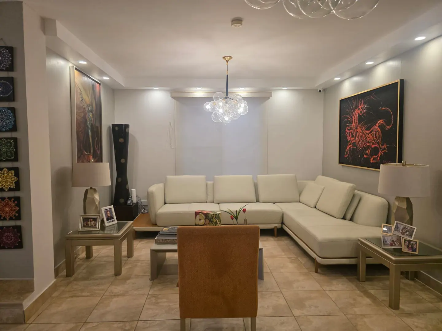 Living room with beige tile floor, white sectional sofa, and modern art. A bubble chandelier hangs from the ceiling.