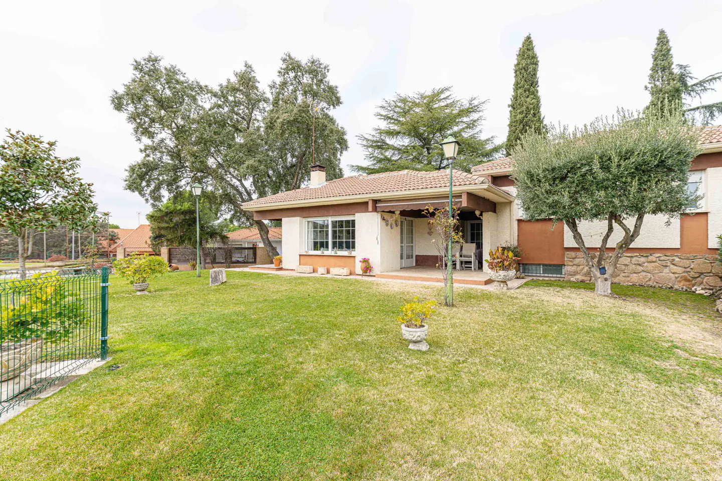 A single-story house with a brown roof and white walls, surrounded by a green lawn and trees.
