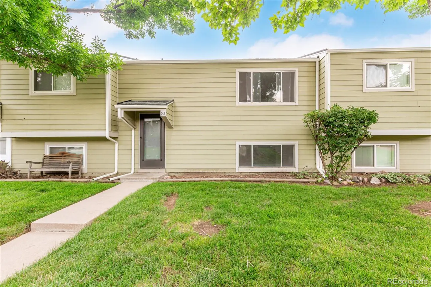 Exterior of a two-story, light green townhouse with a dark front door and a green lawn.