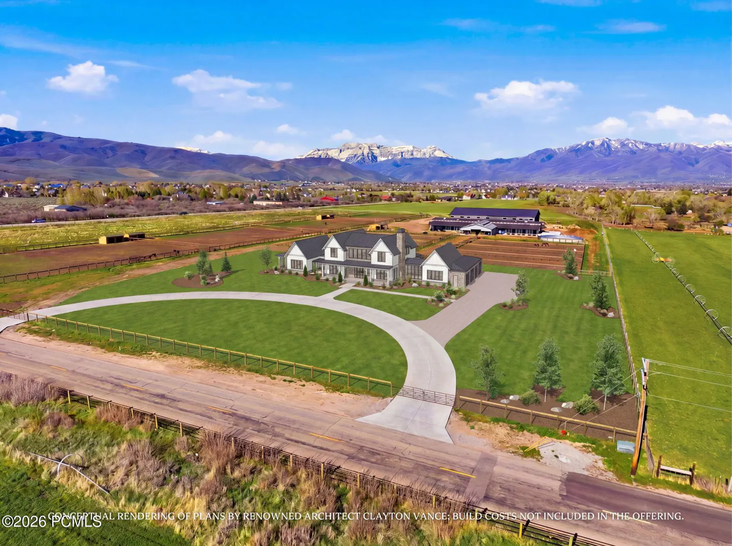 A modern farmhouse with a circular driveway sits on a large green lawn with mountains in the background.