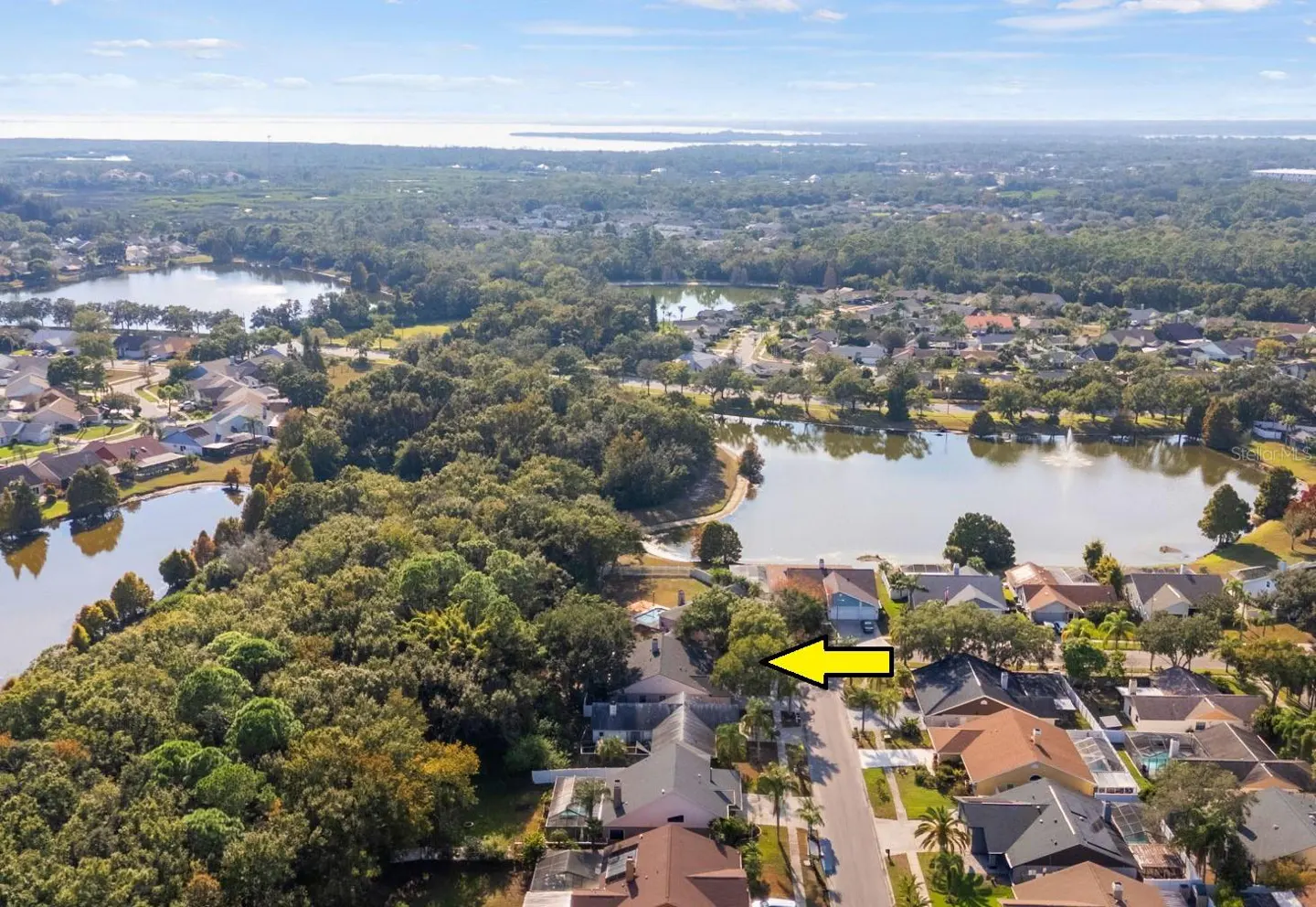 Aerial view of a suburban neighborhood with lakes and trees, indicated by a yellow arrow.
