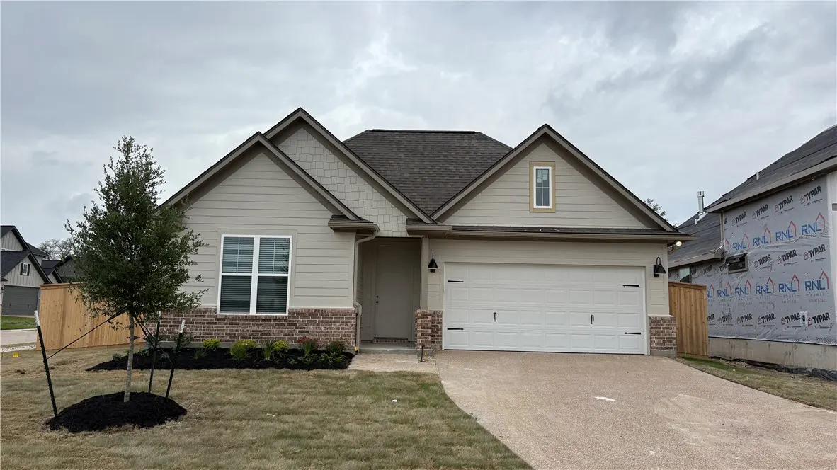 A single-story home with beige siding, a brown roof, and a white garage door on a cloudy day.
