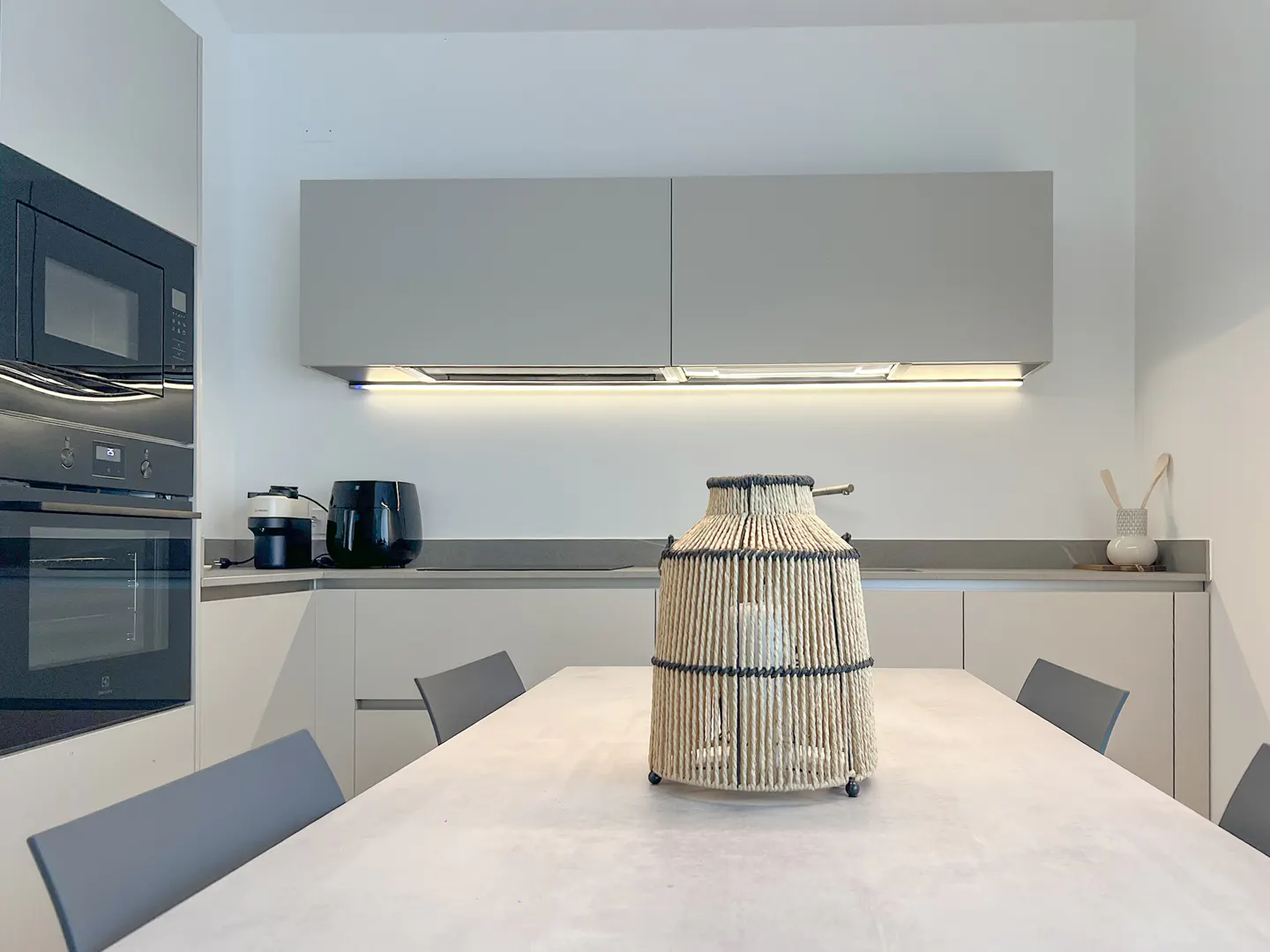 Modern kitchen with light gray cabinets, built-in oven, dining table, and a decorative rope lantern centerpiece.